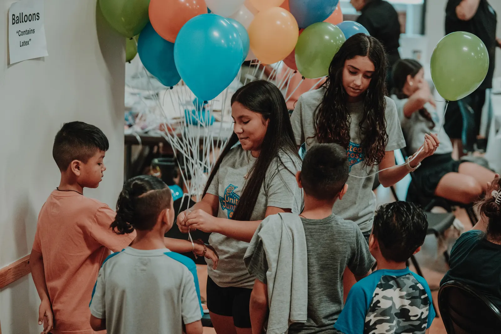 United Juntos teen volunteers handing balloons to children at a community event